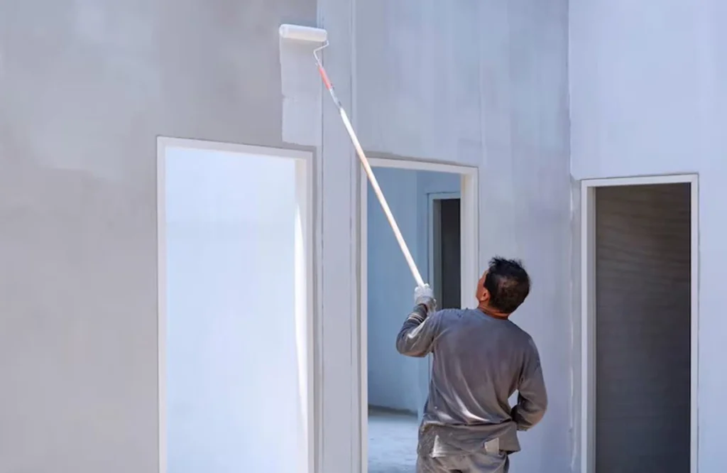 A painter using a roller to apply the best paint for UAE climate on an exterior wall, ensuring durability and protection in extreme heat conditions.