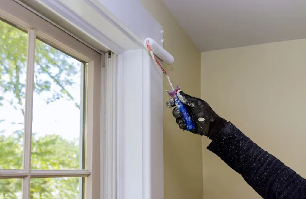 A person applying the best paint for humidity areas in UAE to a window frame. This high-quality paint helps prevent damage caused by moisture, providing long-lasting protection for your walls.