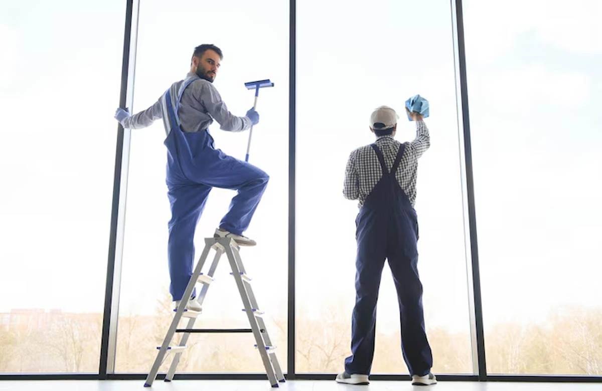 Two specialists clean and prep large glass windows for a commercial painting job. It showcases the precision and care of trusted painting contractors in Dubai.