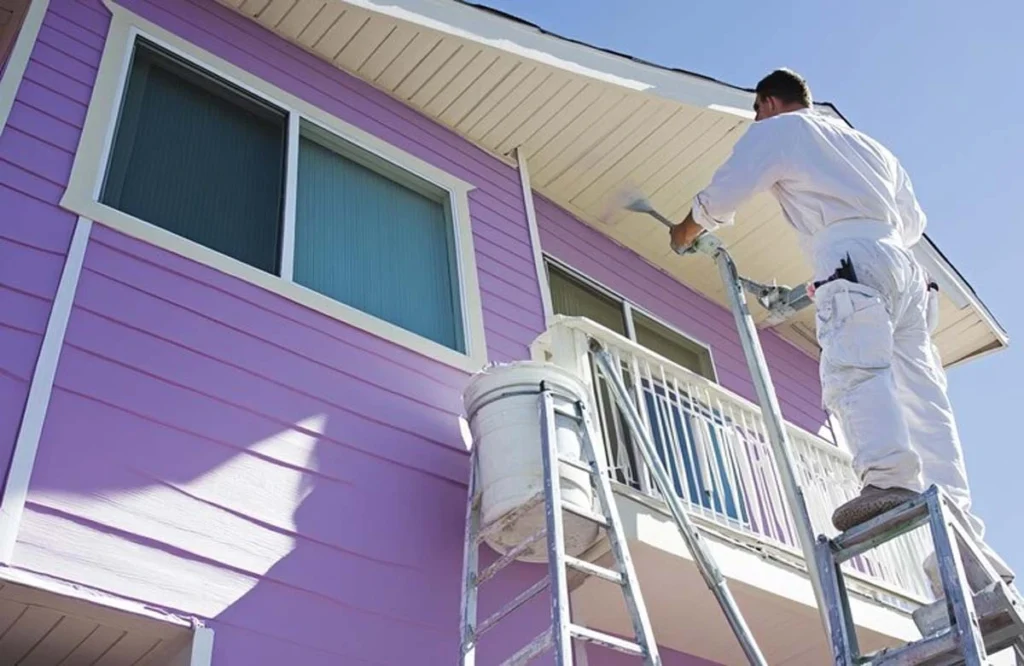 A painter refreshes a villa exterior with a bold purple finish. This vibrant makeover highlights the creative color options available through Villa Painting Services in Dubai.