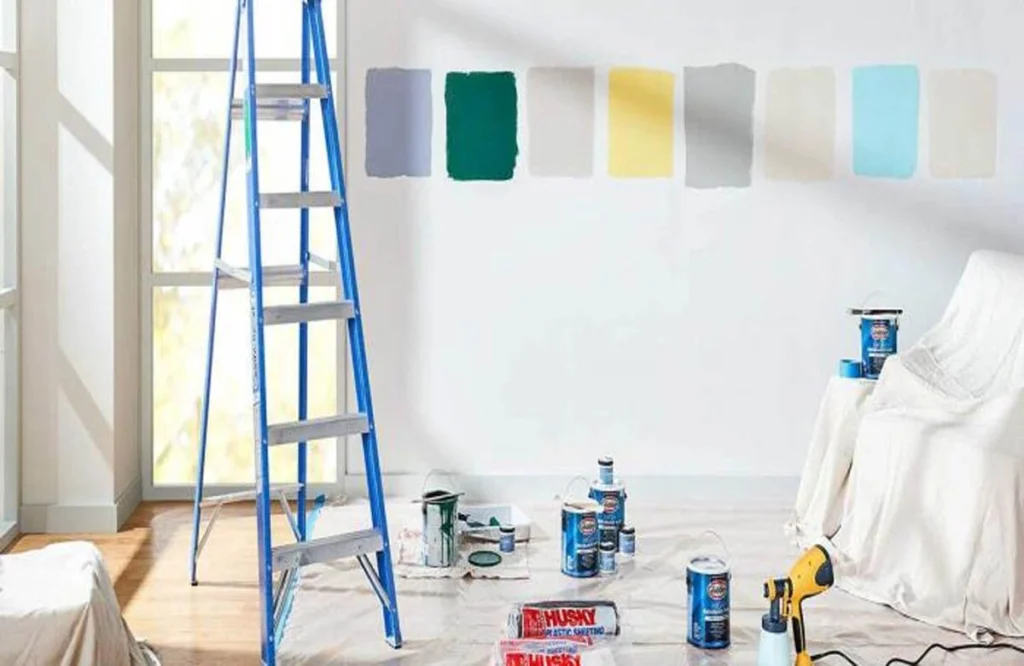 A room prepared by the best painters in Dubai, with color samples on the wall, painting tools, a ladder, and covered furniture.