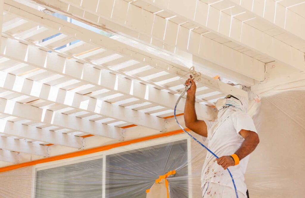 Worker spray-painting wooden beams with precision, showcasing detailed work by Industrial Painting Contractors in Dubai.