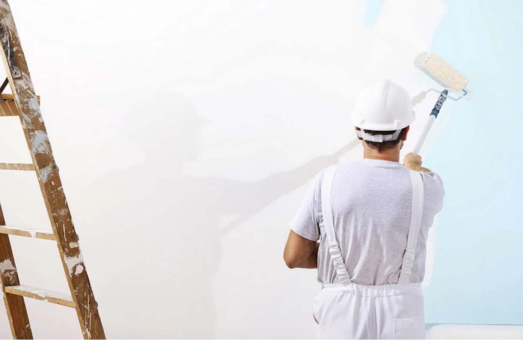 Professional painter in white overalls and helmet using roller to paint a wall — Hire a Painter in Dubai.