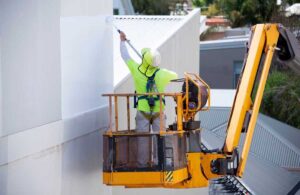 Industrial Painting Contractors in Dubai using a lift to paint the exterior of a high-rise commercial building with precision and safety gear.