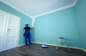 paint finish for Dubai walls | Professional painter in blue overalls painting a teal wall white — quality service by top Interior Paint Companies in Dubai.