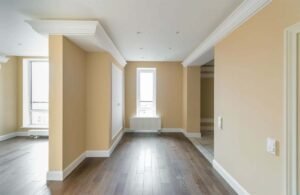 Freshly painted empty room with beige walls, white ceiling molding, and wooden flooring showing results of quality work and reflecting Interior Painting Cost in Dubai.