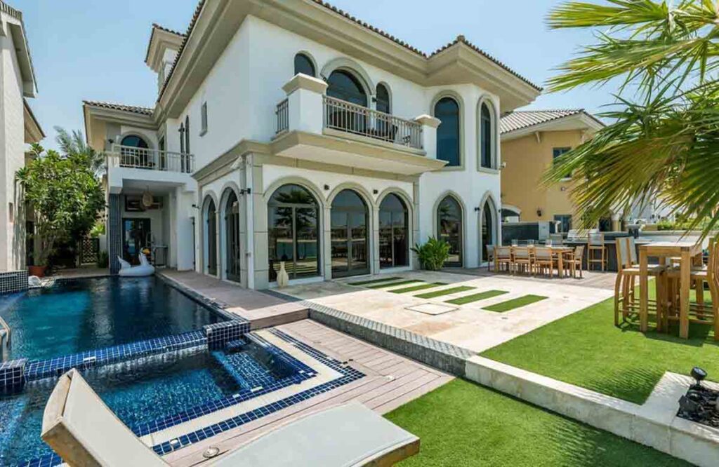 Luxury villa exterior with elegant white wall paint, arched windows, pool, and garden — exterior wall painting Dubai.