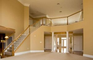 Grand double-height foyer with warm beige walls, white trim, and wooden staircase — a refined look by top Interior Paint Company in Dubai.